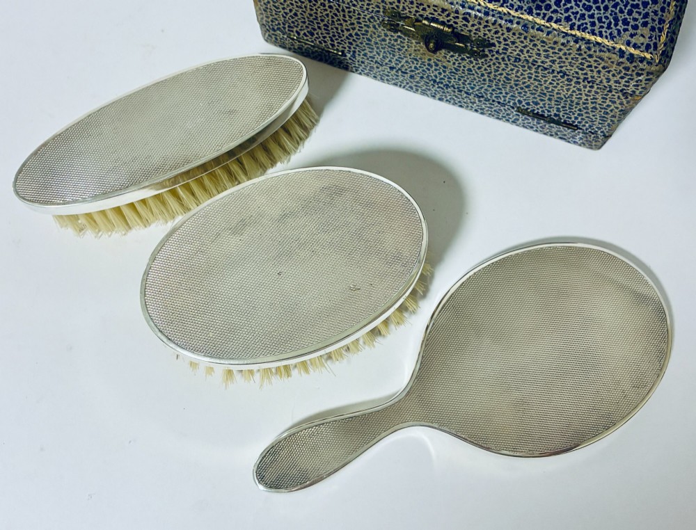 An open blue fitted presentation case displaying two silver-mounted brushes with light-coloured natural bristles against a grey velvet interior. View VI