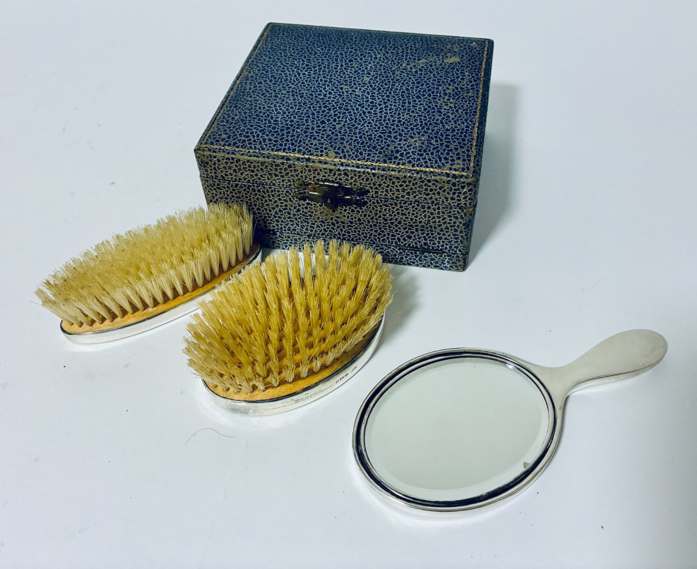 An open blue fitted presentation case displaying two silver-mounted brushes with light-coloured natural bristles against a grey velvet interior. View IX