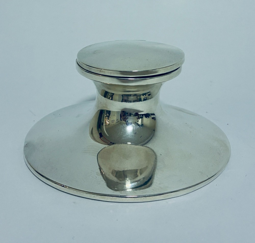 A polished silver capstan inkwell featuring a broad circular base, a tapered central waist, and a hinged flat lid.