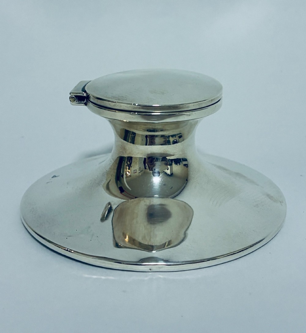 A polished silver capstan inkwell featuring a broad circular base, a tapered central waist, and a hinged flat lid. View V