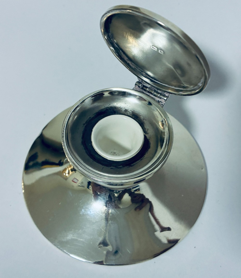 A polished silver capstan inkwell featuring a broad circular base, a tapered central waist, and a hinged flat lid. View X