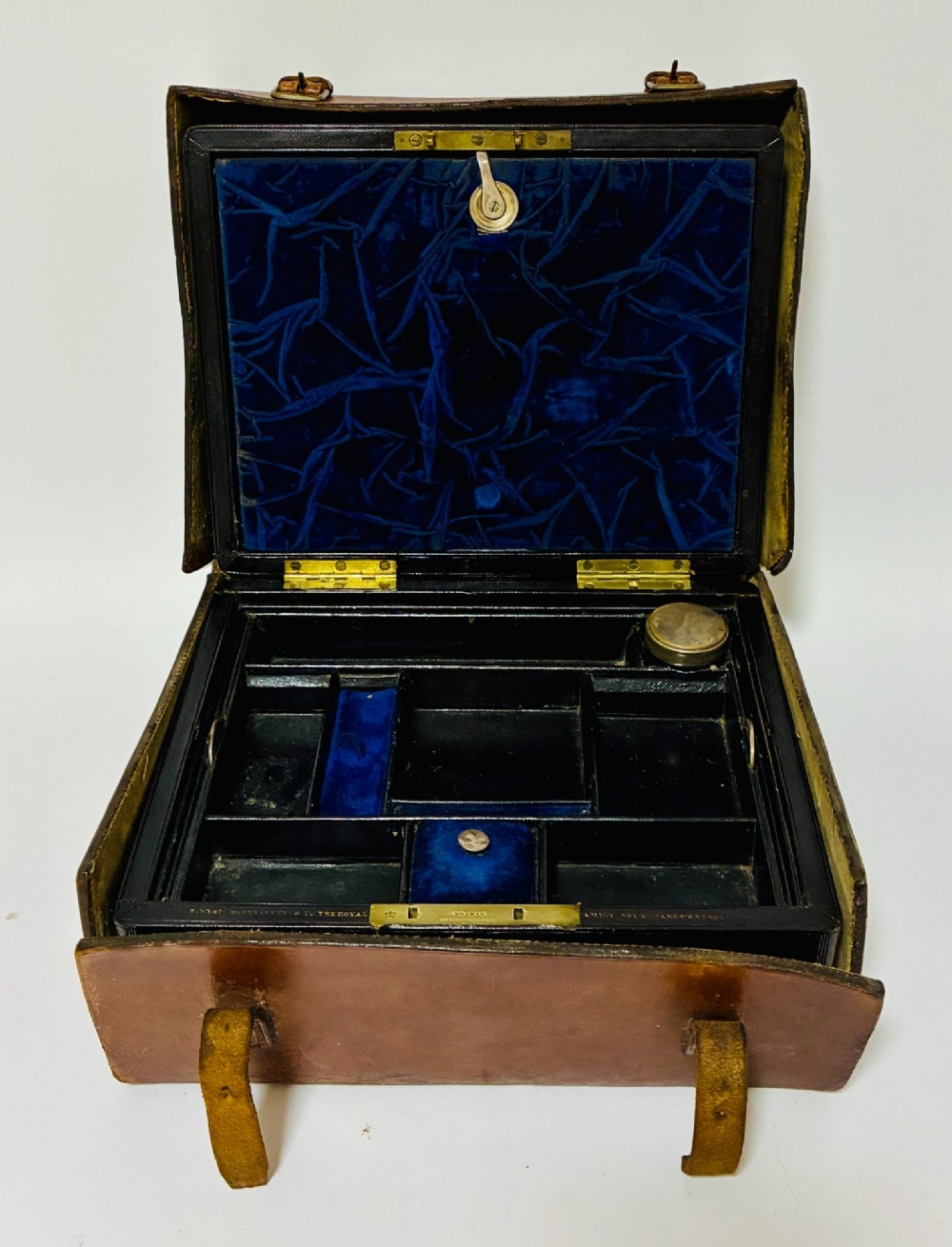 An open Victorian dark brown leather dressing case with a blue velvet-lined lid, brass lock, and compartmentalised interior sitting inside an outer leather travel box.
