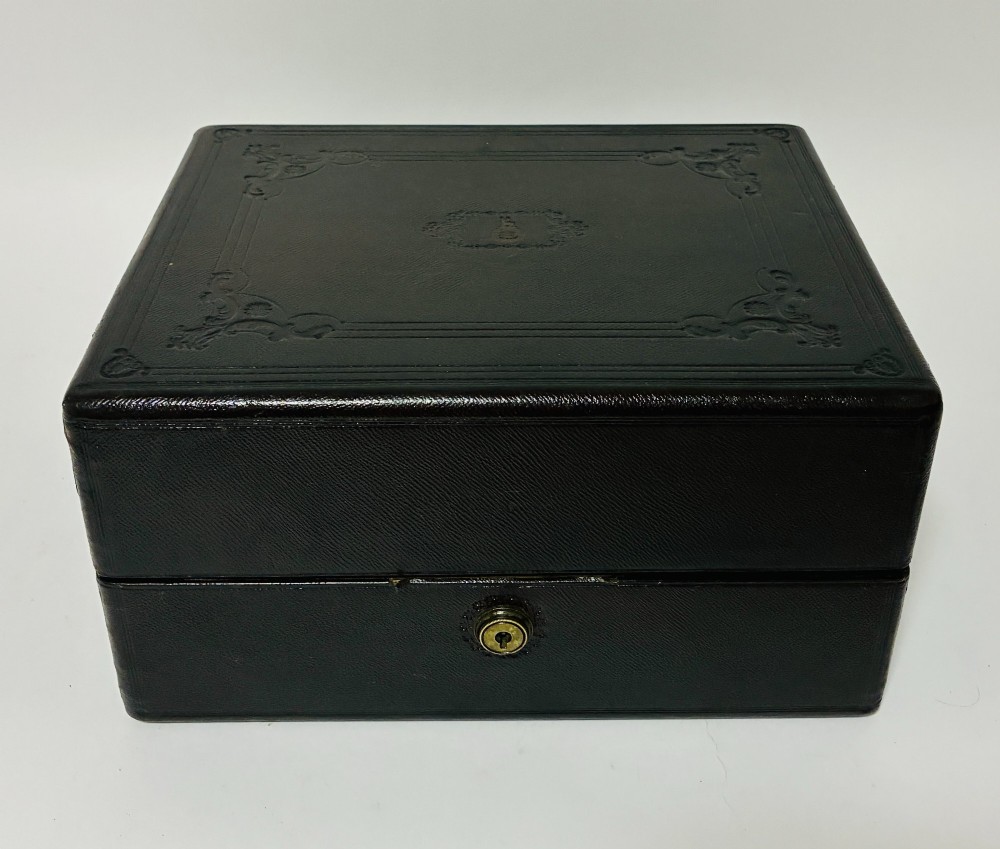An open Victorian dark brown leather dressing case with a blue velvet-lined lid, brass lock, and compartmentalised interior sitting inside an outer leather travel box. View II