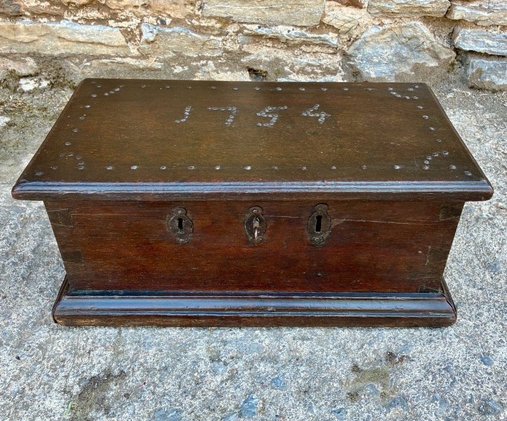 An 18th-century dark oak strong box featuring nail-head studs forming the date 1754 on the lid and three keyholes along the front fascia.