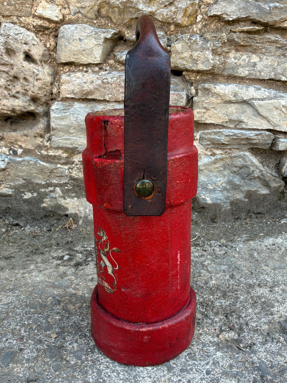 A cylindrical red leather military cordite carrier featuring a hand-painted Royal Coat of Arms and an attached leather handle. View III