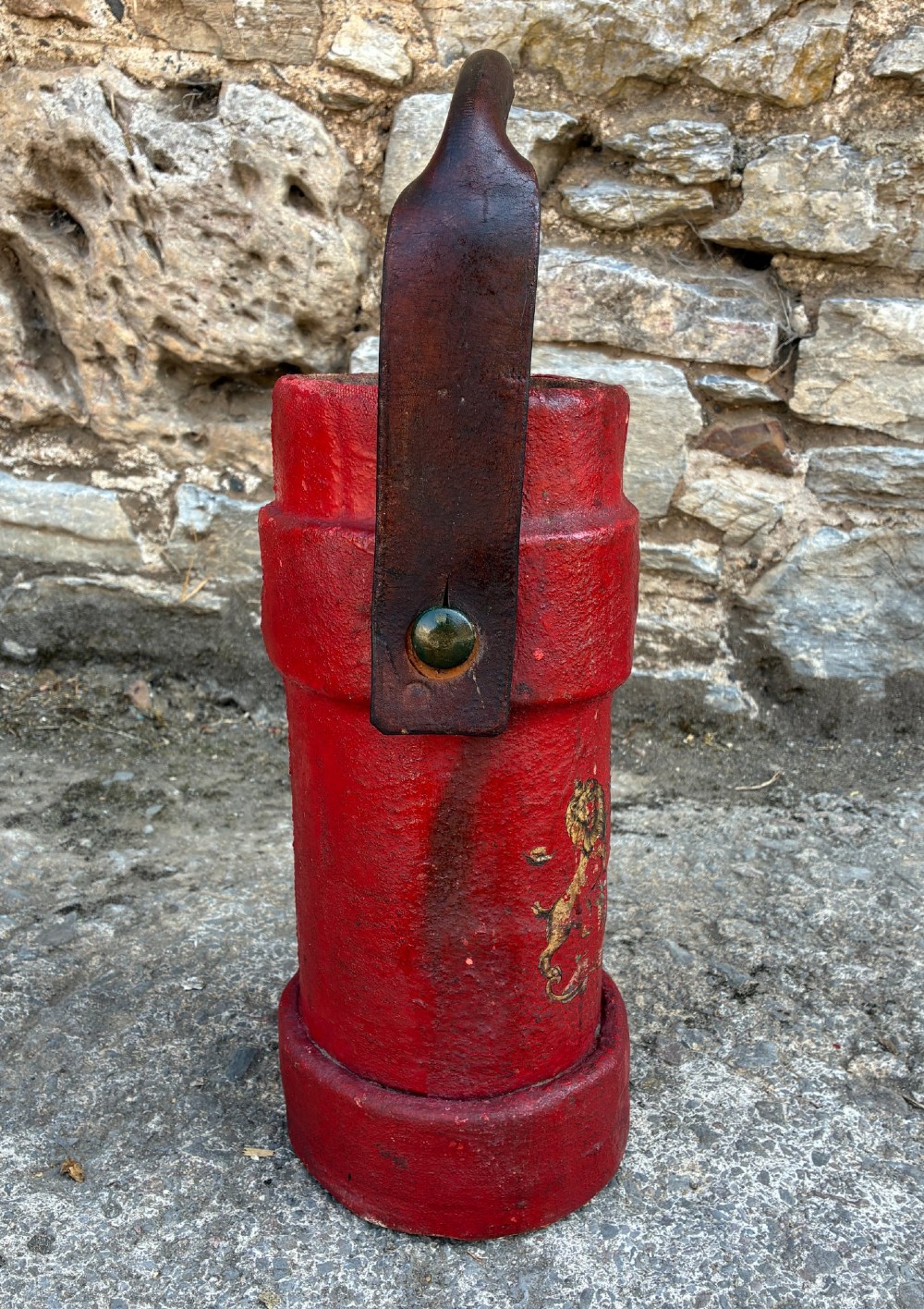 A cylindrical red leather military cordite carrier featuring a hand-painted Royal Coat of Arms and an attached leather handle. View V
