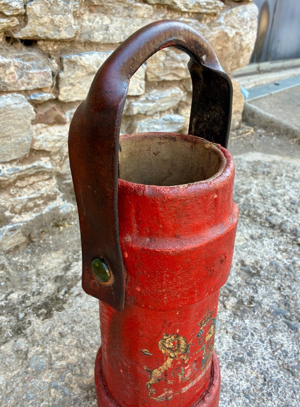 A cylindrical red leather military cordite carrier featuring a hand-painted Royal Coat of Arms and an attached leather handle. View VI