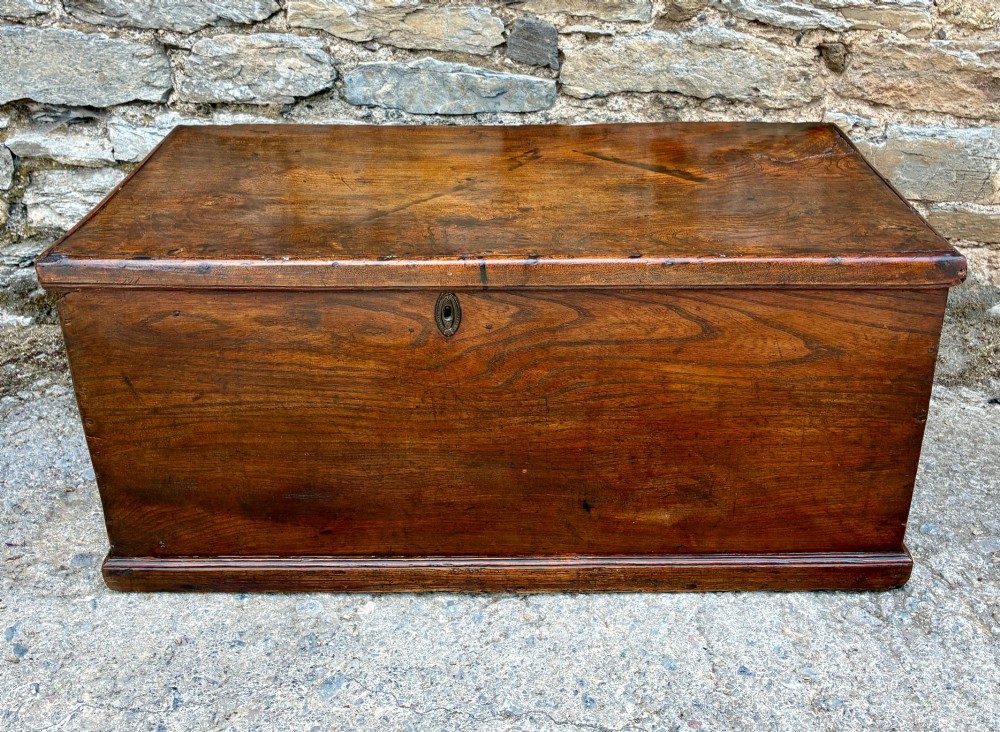 A rectangular antique elm blanket box featuring a hinged lid, visible wood grain, and a central keyhole escutcheon.