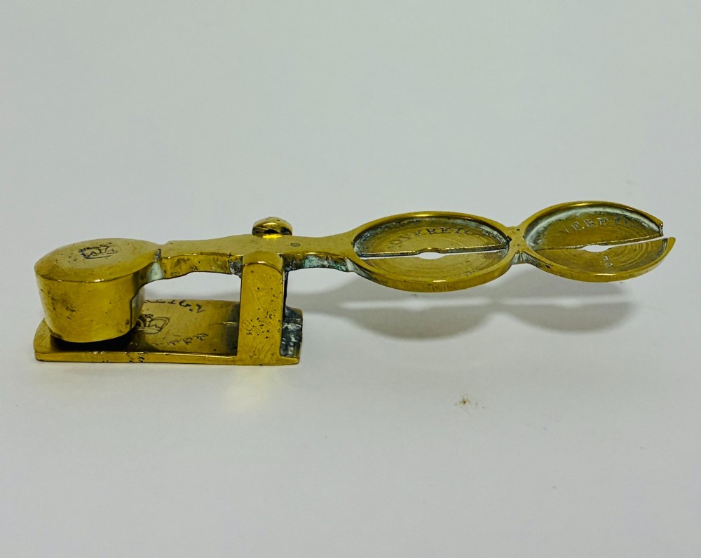 A Victorian brass rocker scale designed for testing gold sovereign coins against a plain white background.