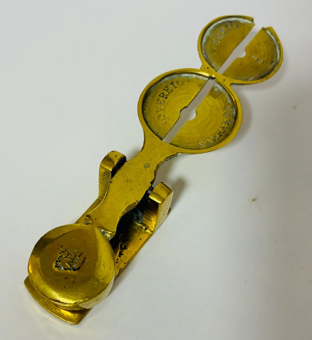 A Victorian brass rocker scale designed for testing gold sovereign coins against a plain white background. View IV