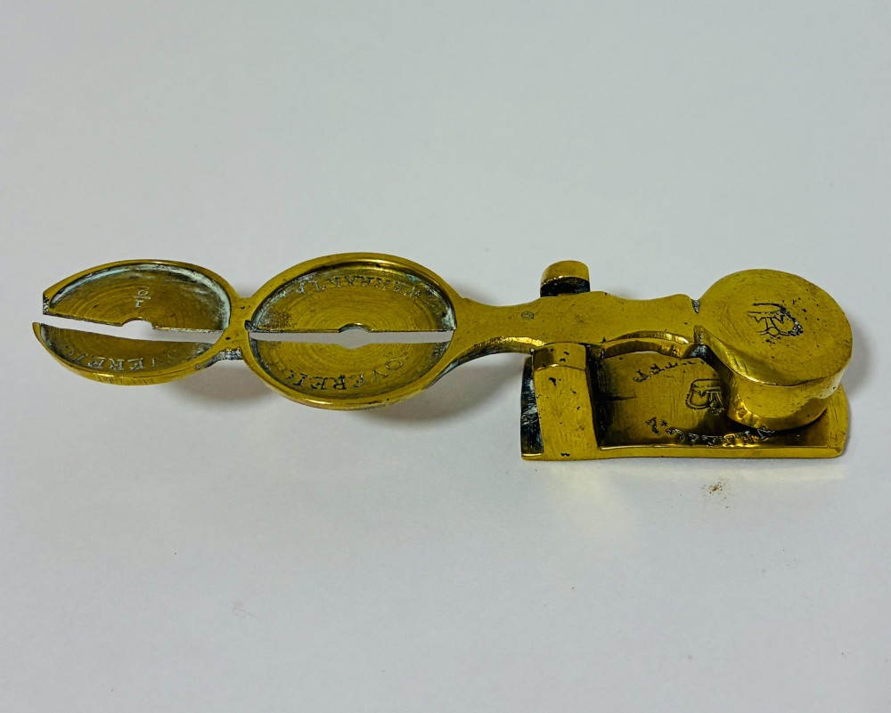A Victorian brass rocker scale designed for testing gold sovereign coins against a plain white background. View V