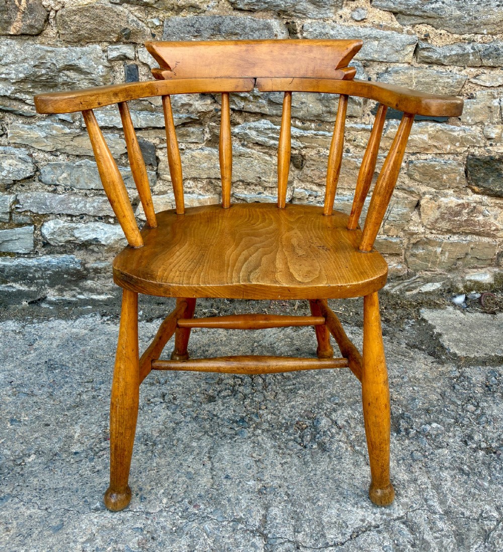 An antique elm captains armchair featuring turned spindles, a low curved backrest, a carved saddle seat, and turned legs with stretchers. View II
