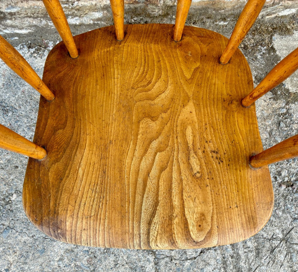 An antique elm captains armchair featuring turned spindles, a low curved backrest, a carved saddle seat, and turned legs with stretchers. View III