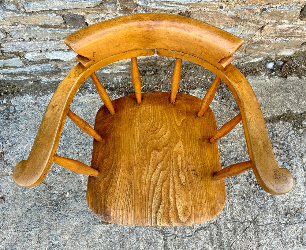 An antique elm captains armchair featuring turned spindles, a low curved backrest, a carved saddle seat, and turned legs with stretchers. View IV