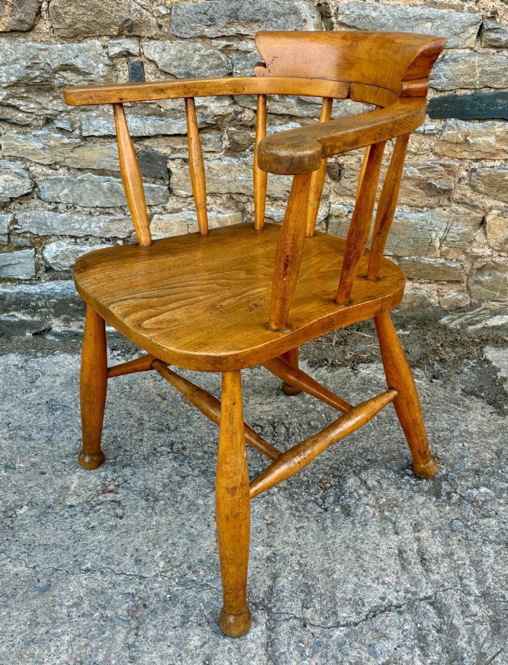 An antique elm captains armchair featuring turned spindles, a low curved backrest, a carved saddle seat, and turned legs with stretchers. View V