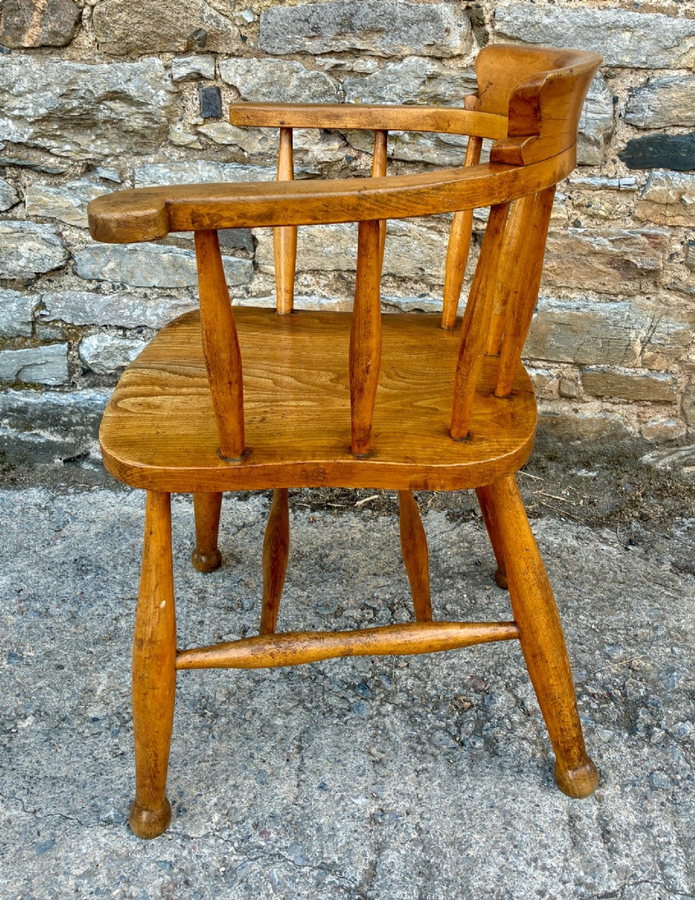 An antique elm captains armchair featuring turned spindles, a low curved backrest, a carved saddle seat, and turned legs with stretchers. View VI