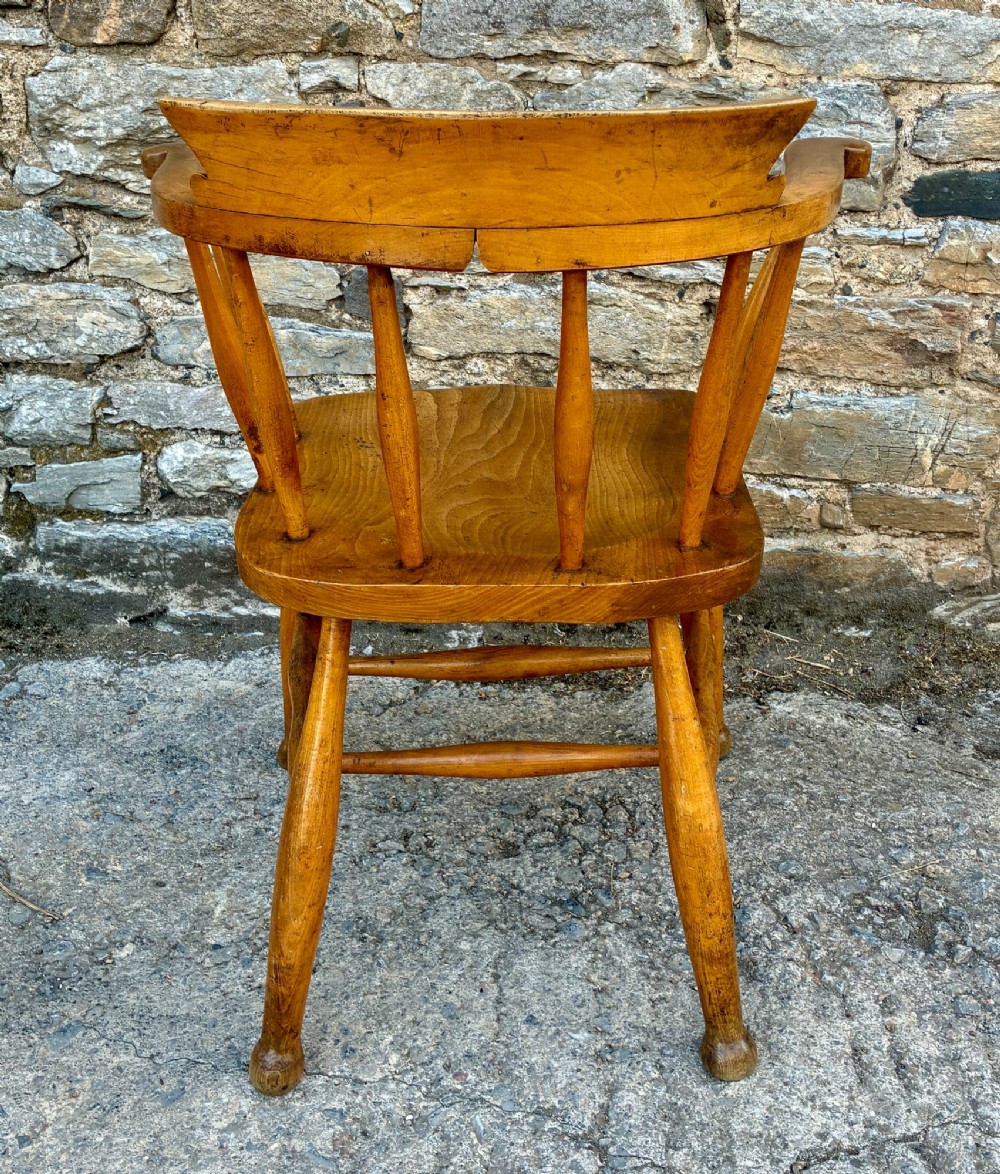 An antique elm captains armchair featuring turned spindles, a low curved backrest, a carved saddle seat, and turned legs with stretchers. View VII