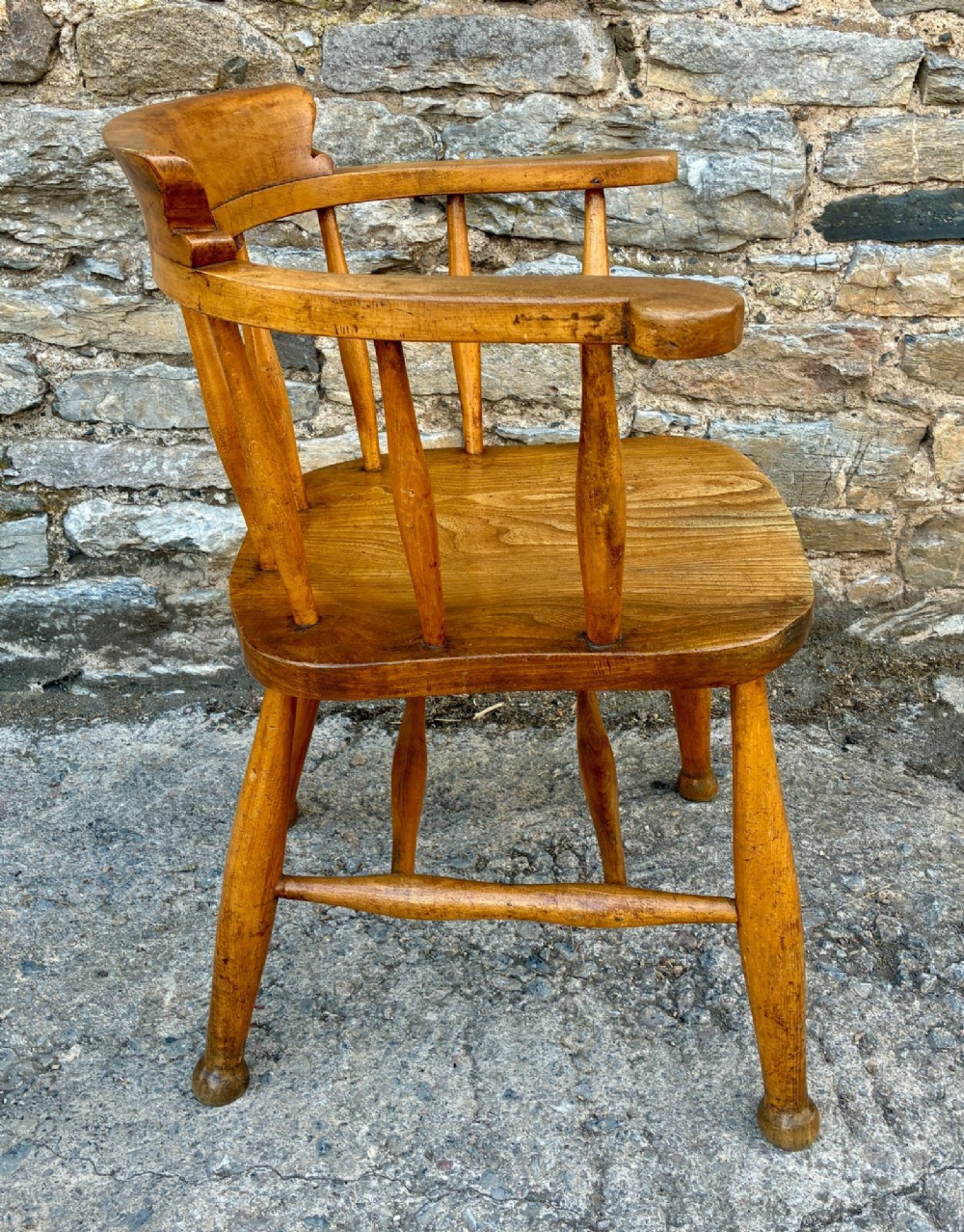 An antique elm captains armchair featuring turned spindles, a low curved backrest, a carved saddle seat, and turned legs with stretchers. View VIII
