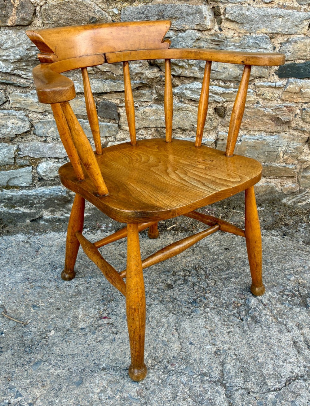 An antique elm captains armchair featuring turned spindles, a low curved backrest, a carved saddle seat, and turned legs with stretchers. View IX