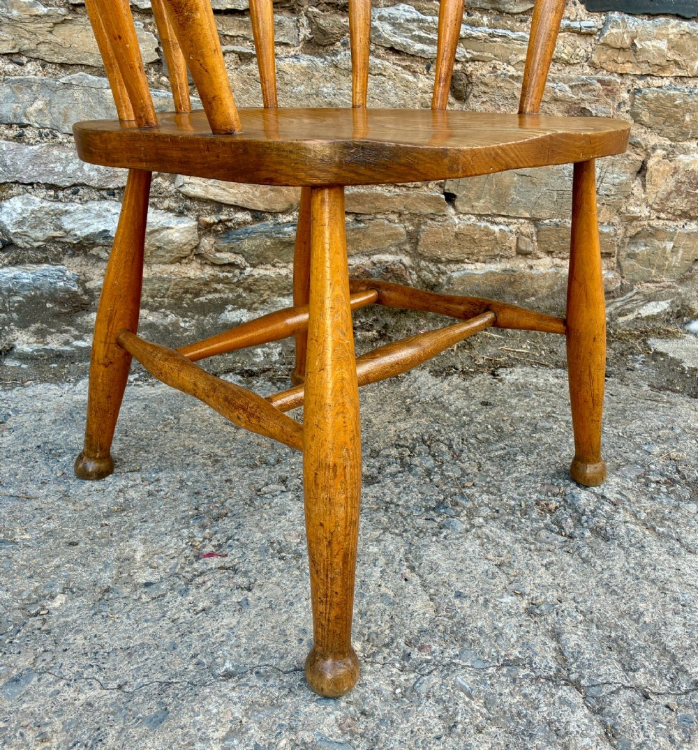 An antique elm captains armchair featuring turned spindles, a low curved backrest, a carved saddle seat, and turned legs with stretchers. View X