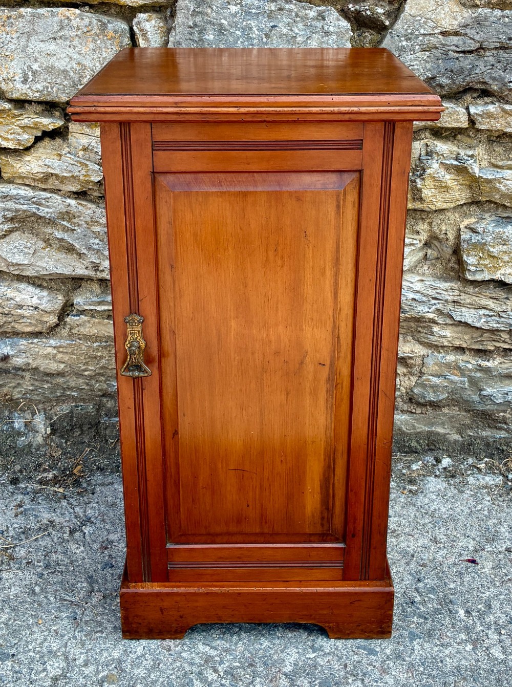 An Edwardian warm brown walnut pot cupboard featuring a single panelled door with a brass handle and reeded side moulding.