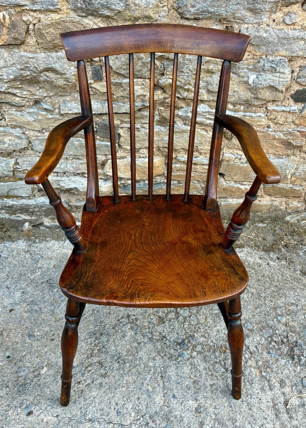 An antique dark brown wooden stick back Windsor armchair with turned legs, curved armrests, and a shaped solid elm seat. View II