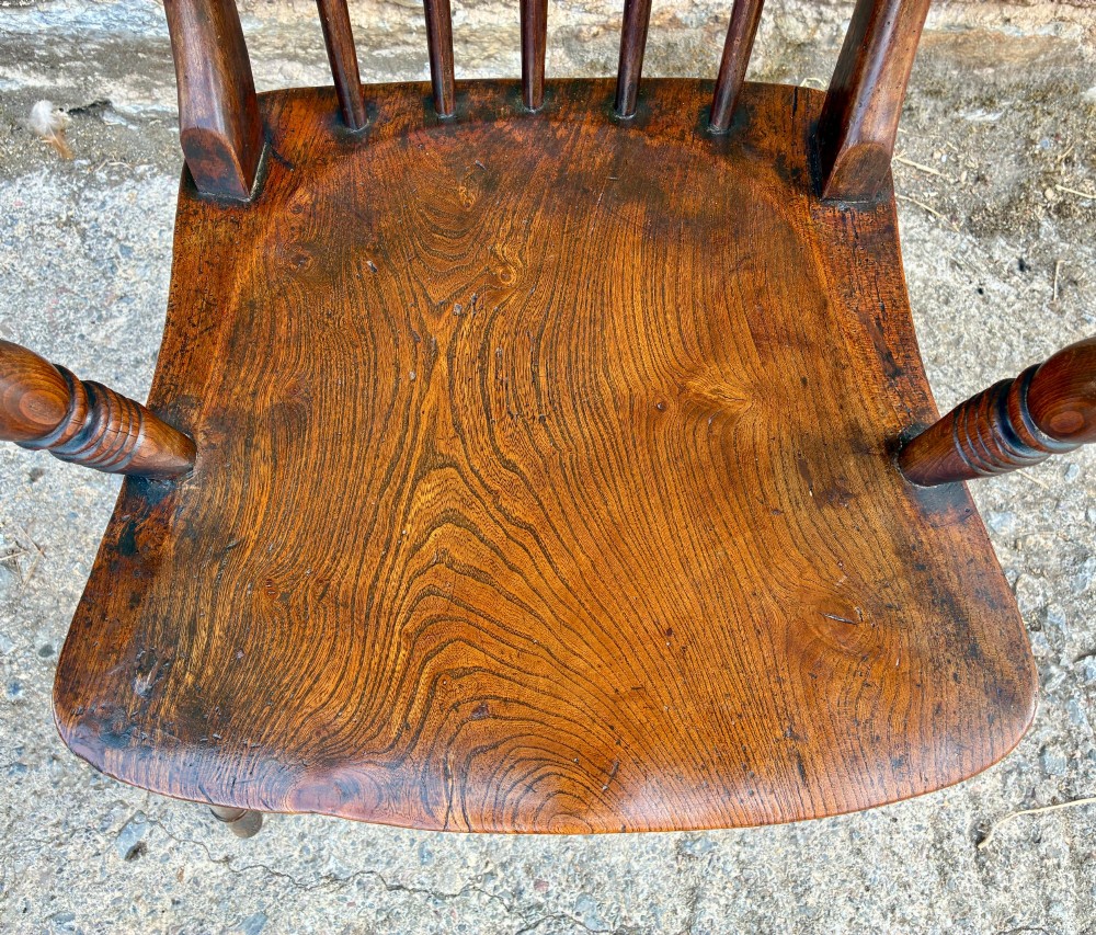 An antique dark brown wooden stick back Windsor armchair with turned legs, curved armrests, and a shaped solid elm seat. View III