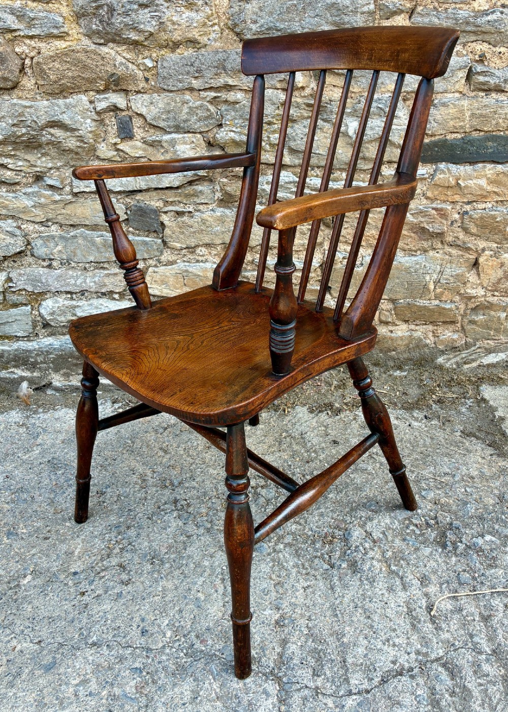 An antique dark brown wooden stick back Windsor armchair with turned legs, curved armrests, and a shaped solid elm seat. View IV