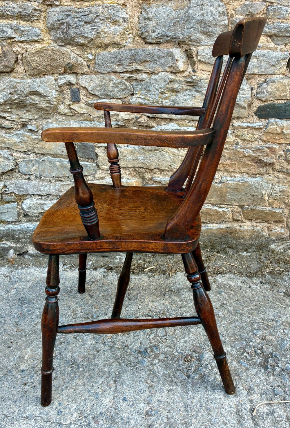 An antique dark brown wooden stick back Windsor armchair with turned legs, curved armrests, and a shaped solid elm seat. View V