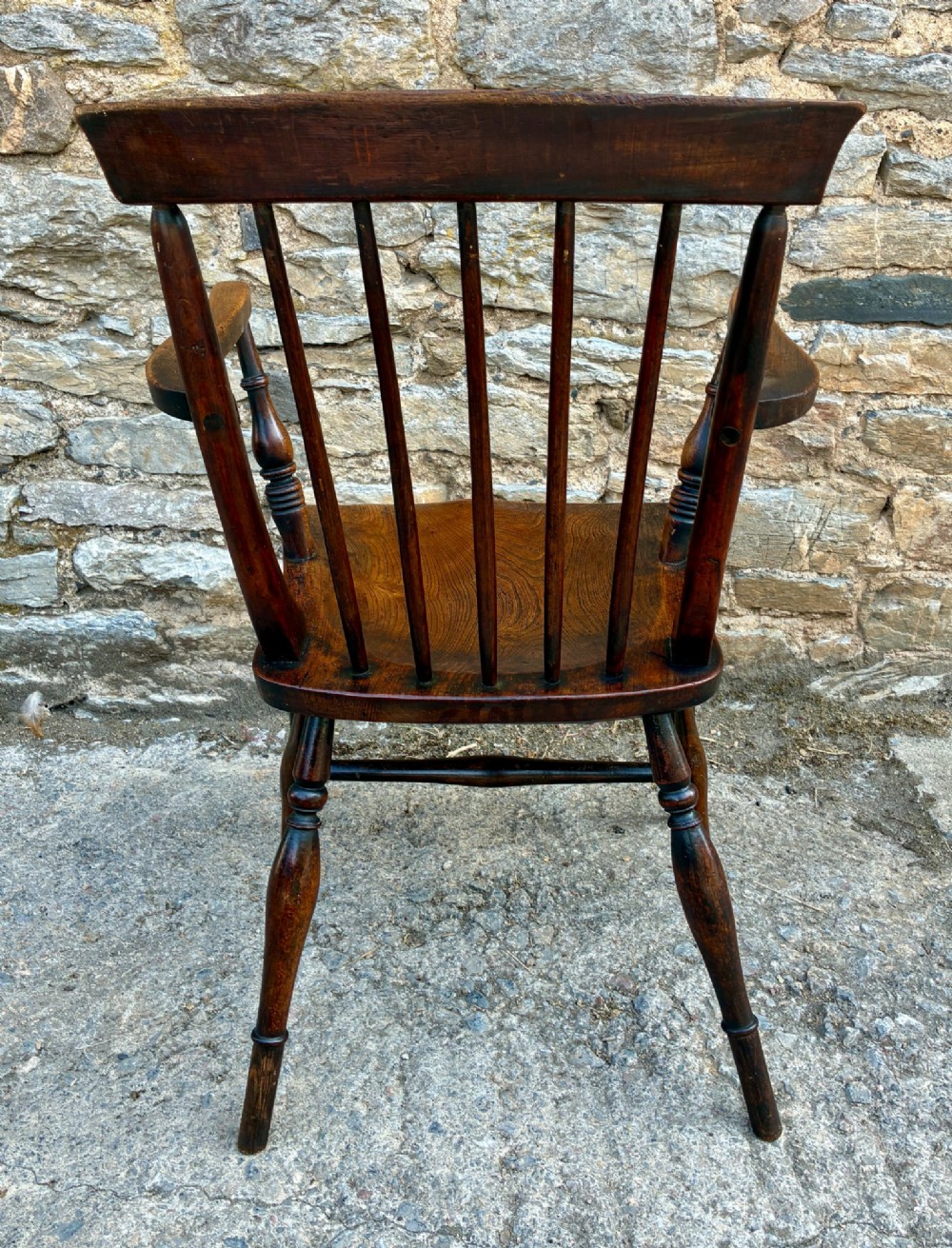 An antique dark brown wooden stick back Windsor armchair with turned legs, curved armrests, and a shaped solid elm seat. View VI