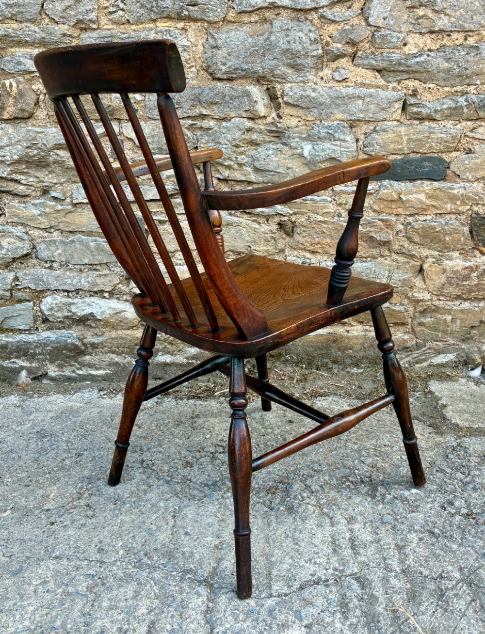 An antique dark brown wooden stick back Windsor armchair with turned legs, curved armrests, and a shaped solid elm seat. View VII