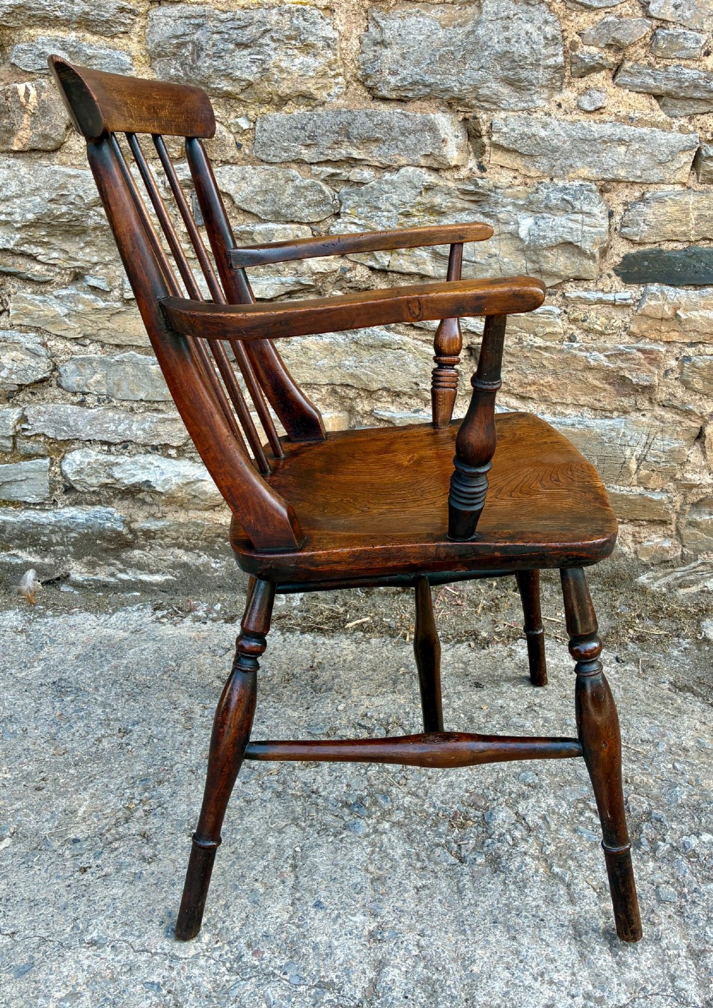 An antique dark brown wooden stick back Windsor armchair with turned legs, curved armrests, and a shaped solid elm seat. View VIII