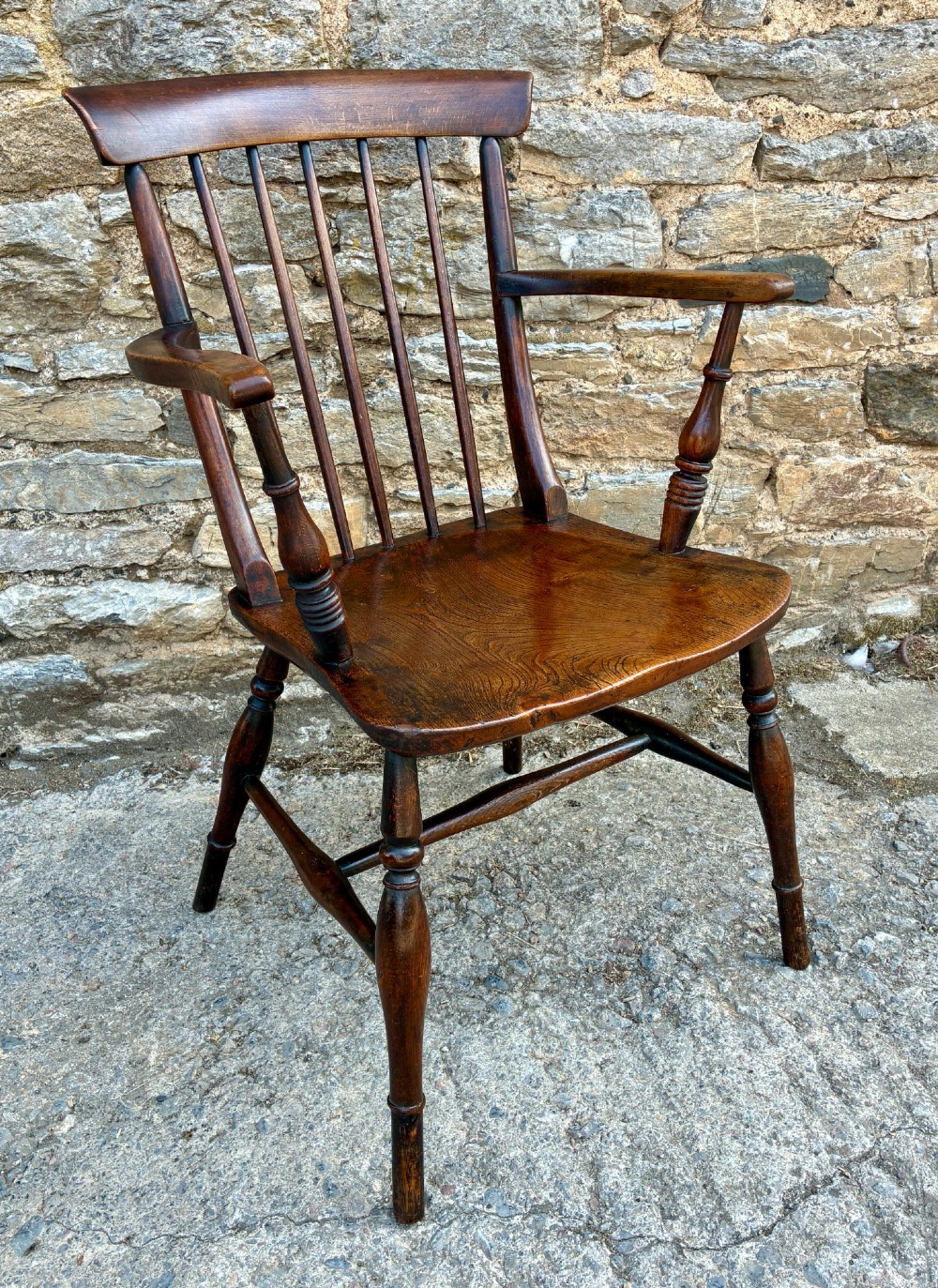An antique dark brown wooden stick back Windsor armchair with turned legs, curved armrests, and a shaped solid elm seat. View IX