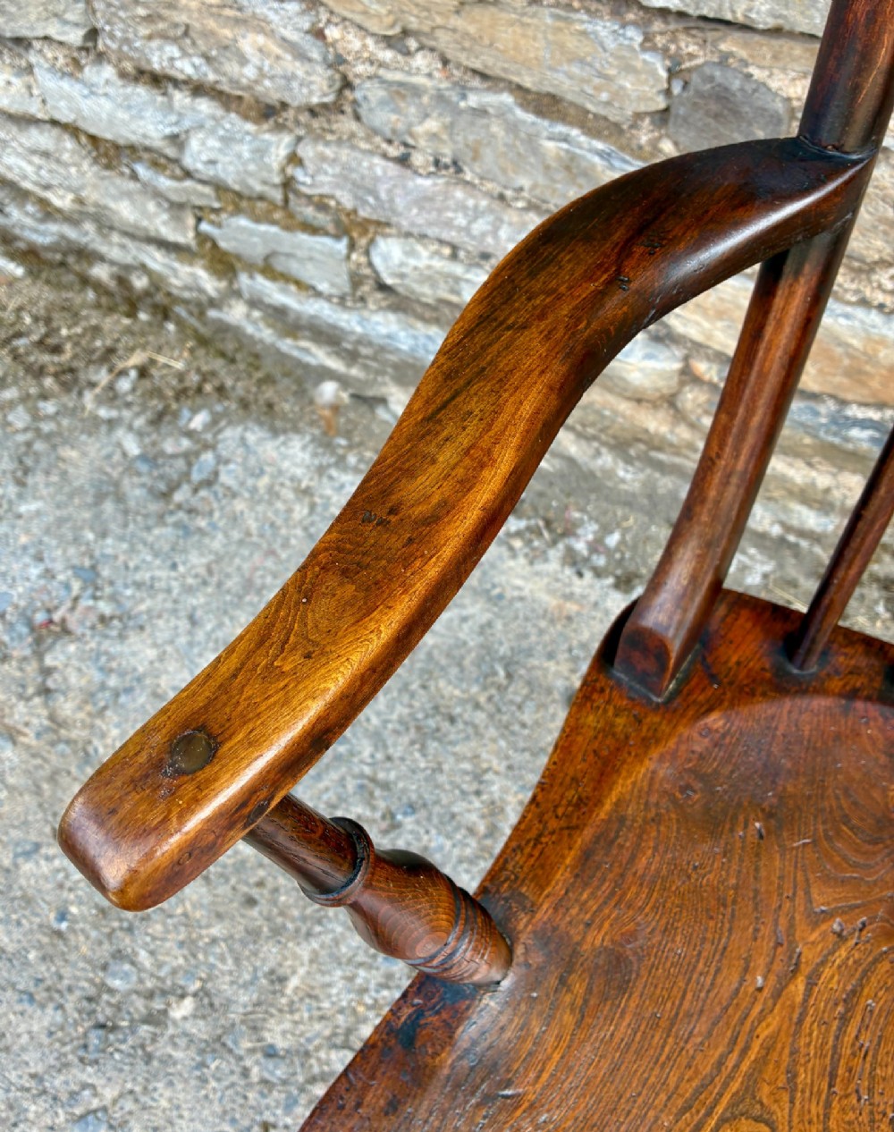 An antique dark brown wooden stick back Windsor armchair with turned legs, curved armrests, and a shaped solid elm seat. View XI