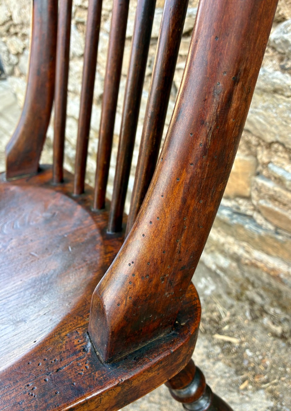 An antique dark brown wooden stick back Windsor armchair with turned legs, curved armrests, and a shaped solid elm seat. View XIII