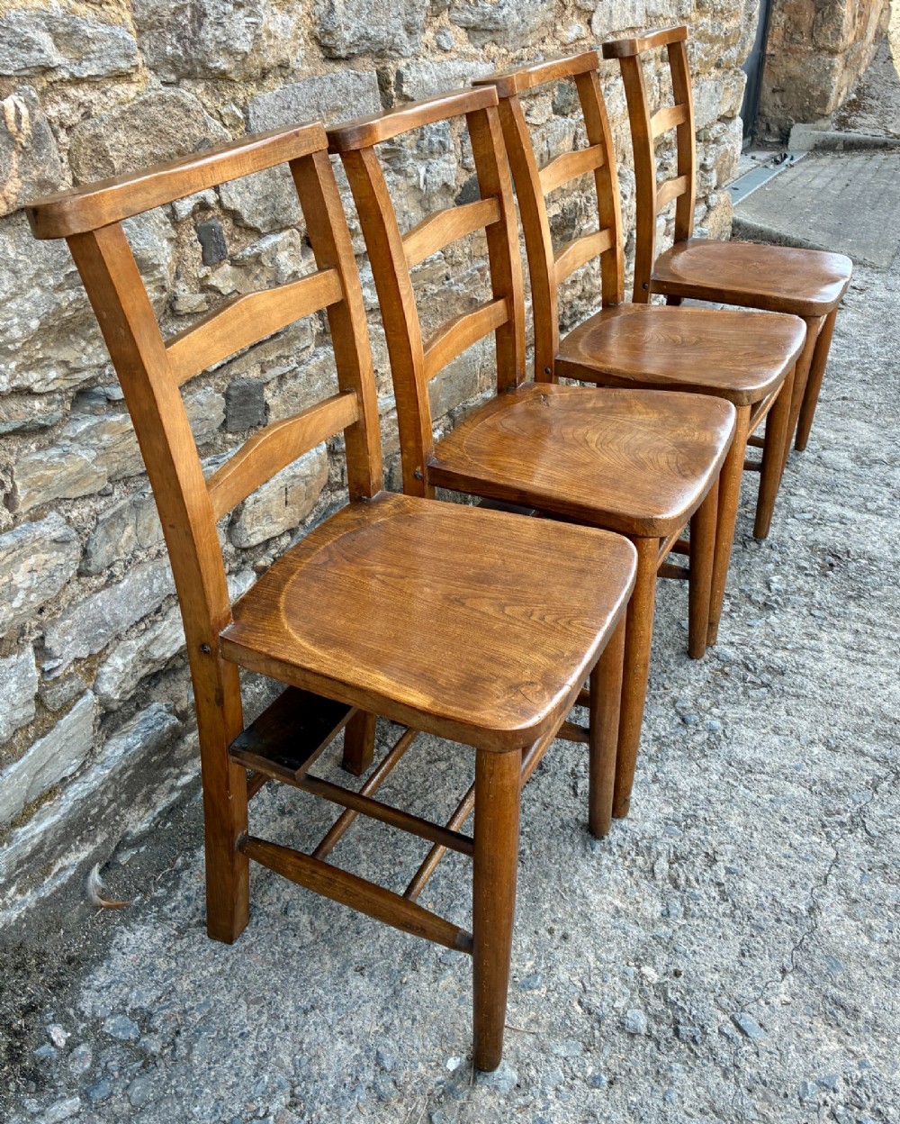 A set of four matching antique wooden chapel chairs with contoured seats and ladder-back rails. View IV