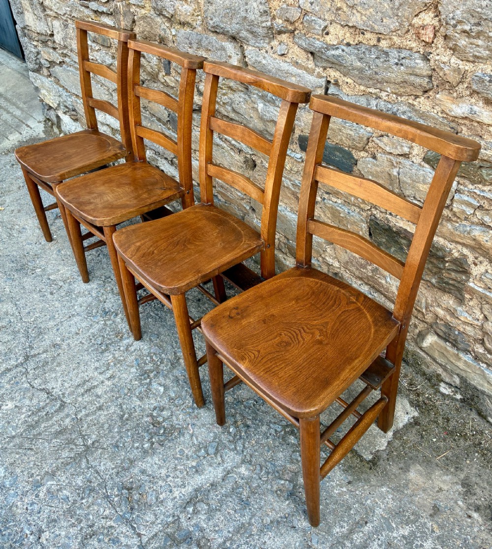 A set of four matching antique wooden chapel chairs with contoured seats and ladder-back rails. View V