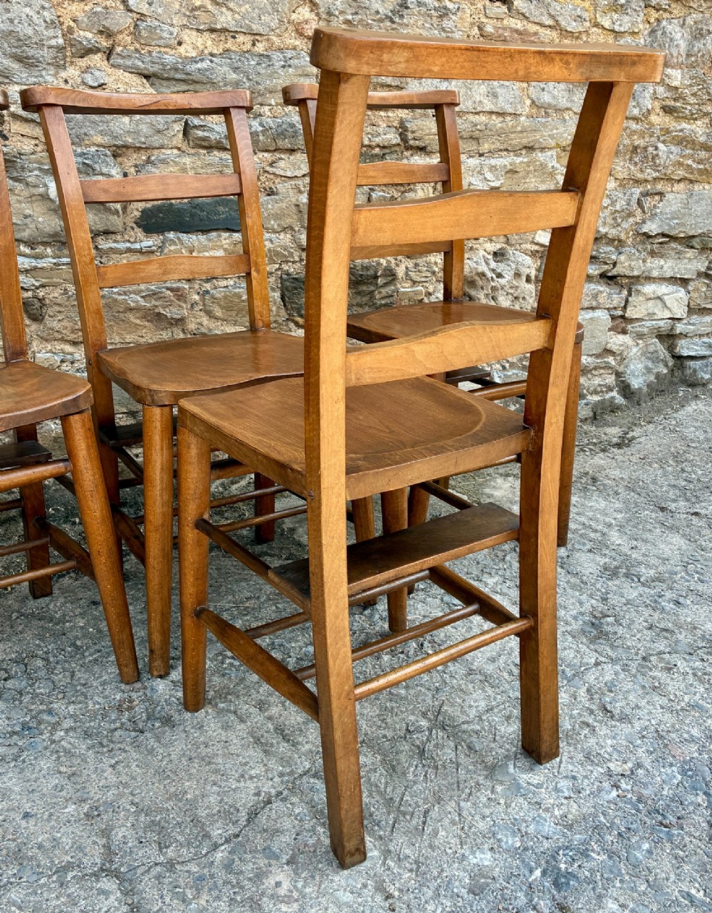 A set of four matching antique wooden chapel chairs with contoured seats and ladder-back rails. View X
