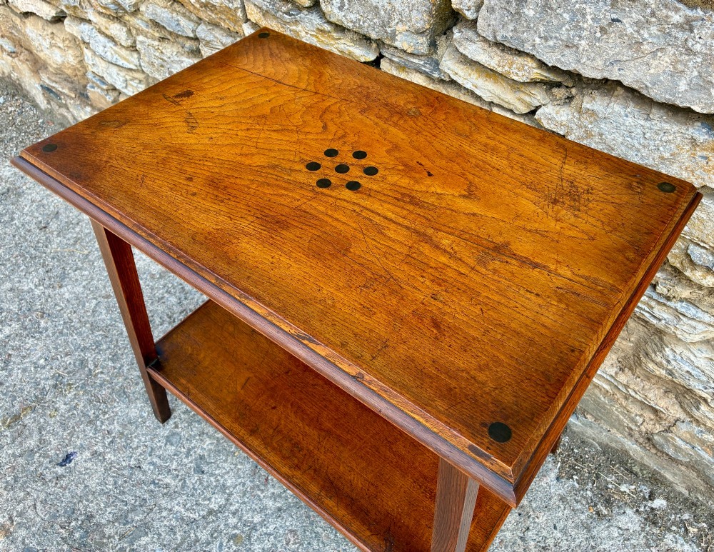 An Arts and Crafts solid oak side table featuring a lower shelf, straight square legs, and dark circular wood inlays arranged in a grid pattern on the top surface. View V