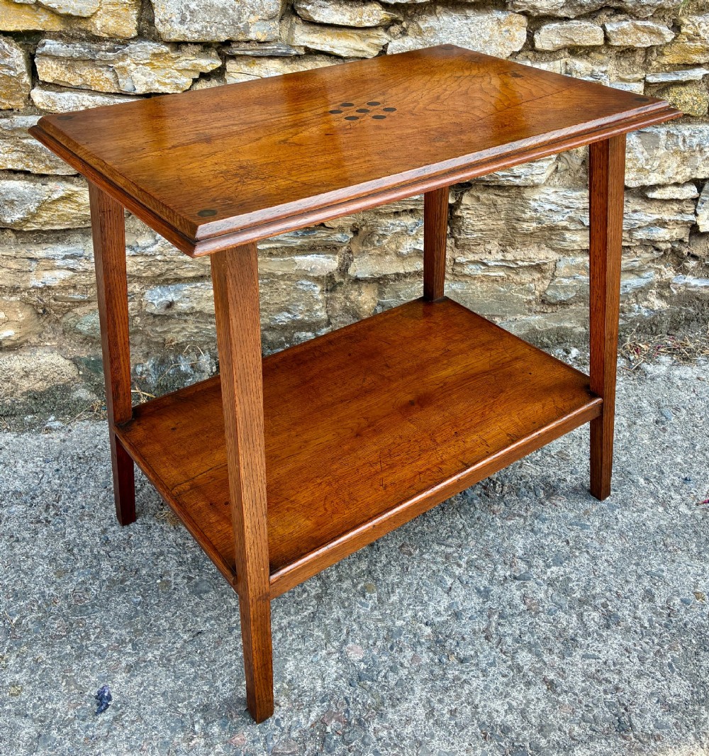 An Arts and Crafts solid oak side table featuring a lower shelf, straight square legs, and dark circular wood inlays arranged in a grid pattern on the top surface. View IX