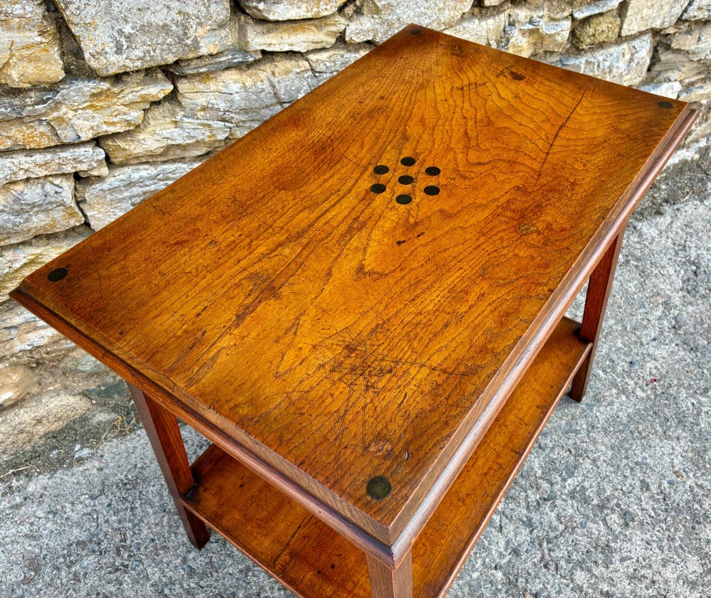 An Arts and Crafts solid oak side table featuring a lower shelf, straight square legs, and dark circular wood inlays arranged in a grid pattern on the top surface. View X