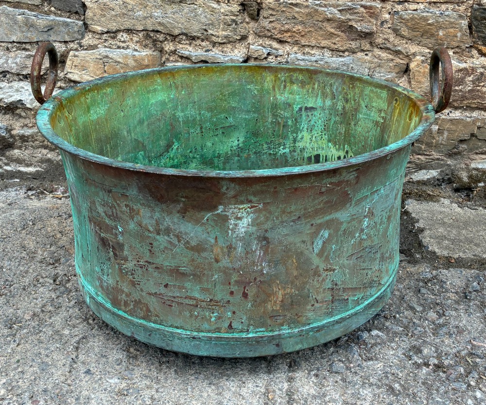A large circular antique copper wash tub displaying heavy green verdigris oxidisation and two iron side handles.
