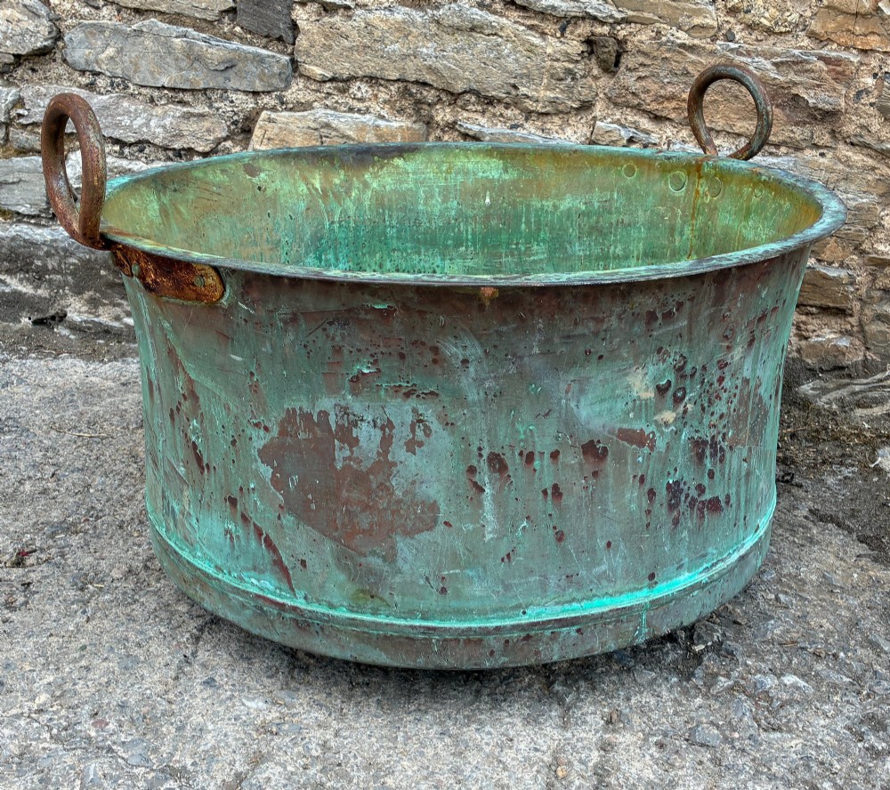 A large circular antique copper wash tub displaying heavy green verdigris oxidisation and two iron side handles. View VIII