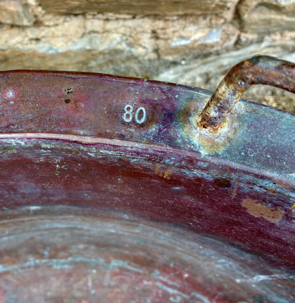 A large, circular antique copper wash tub featuring twin wrought iron carrying handles, a rolled rim, and heavy surface oxidisation with verdigris. View V