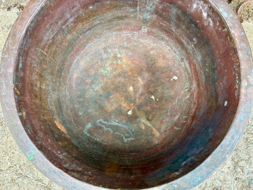 A large, circular antique copper wash tub featuring twin wrought iron carrying handles, a rolled rim, and heavy surface oxidisation with verdigris. View VI