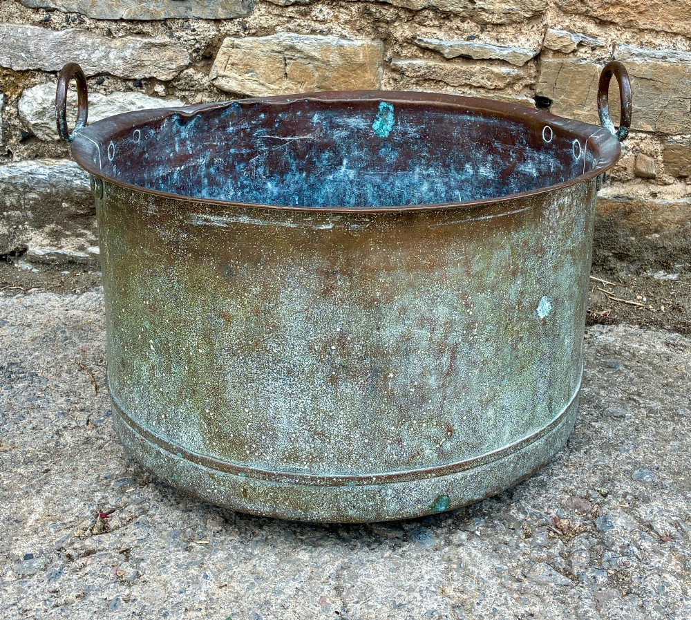 A large cylindrical antique copper wash tub featuring a flared rolled rim, side handles, and a heavily aged green verdigris patina.