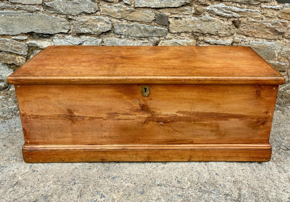 A rectangular pine blanket box featuring a hinged lid, brass keyhole escutcheon, and a low plinth base.