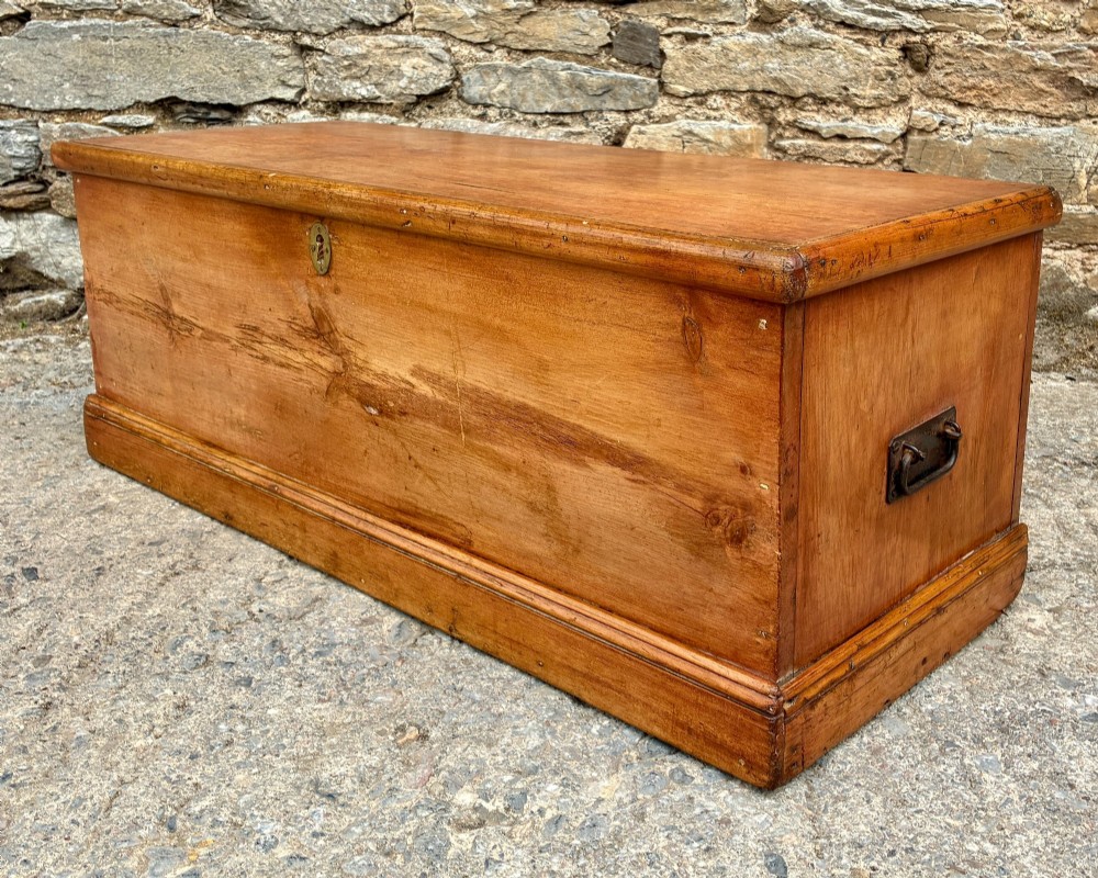 A rectangular pine blanket box featuring a hinged lid, brass keyhole escutcheon, and a low plinth base. View VII