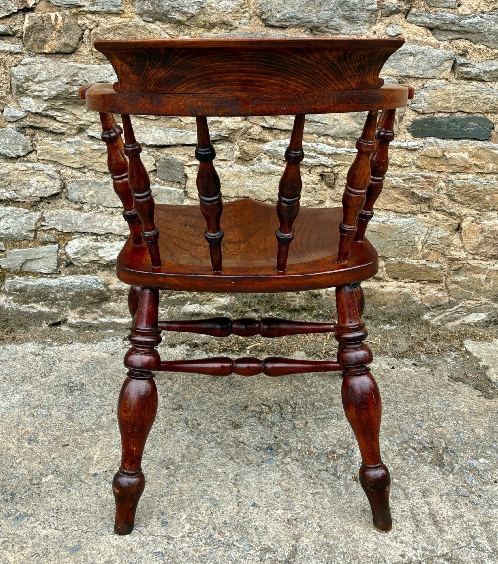 An antique warm brown elm captains chair with turned spindles, a contoured saddle seat, and turned legs connected by stretchers. View VI