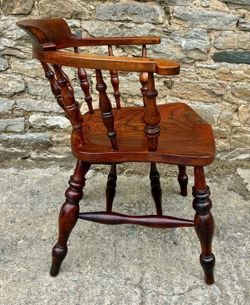An antique warm brown elm captains chair with turned spindles, a contoured saddle seat, and turned legs connected by stretchers. View IX